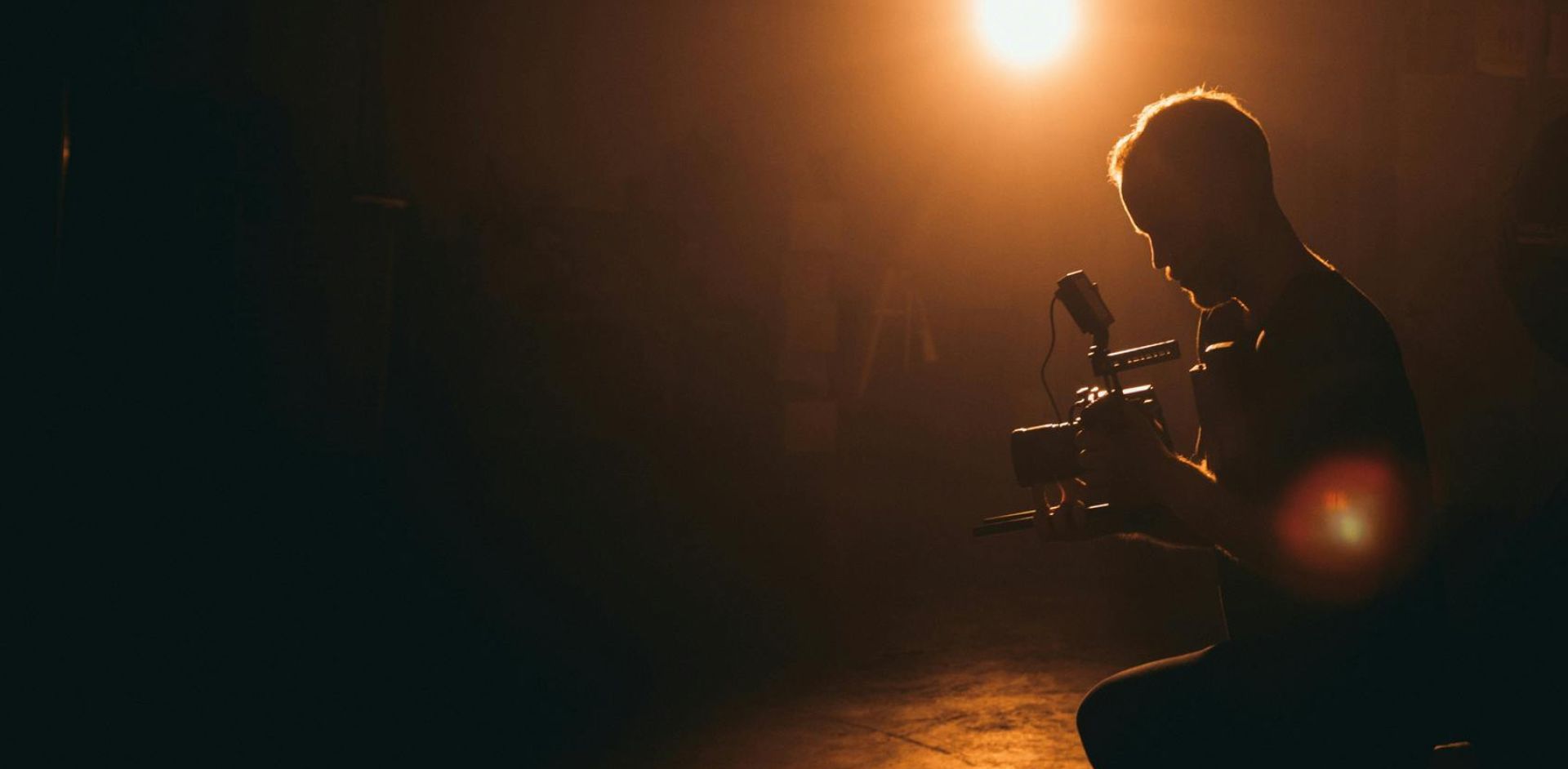 Silhouette of a cinematographer operating a camera in a dimly lit studio with dramatic lighting.